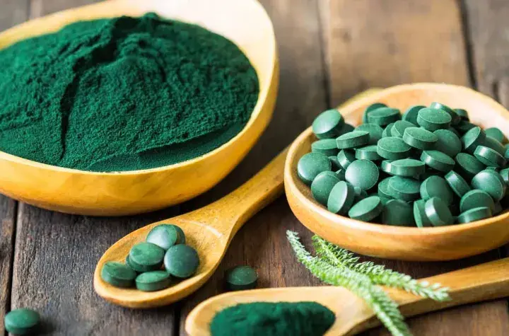 Polvo y pastillas verdes vibrantes, que muestran qué es la chlorella, en cuencos de madera y cucharas sobre una superficie rústica.