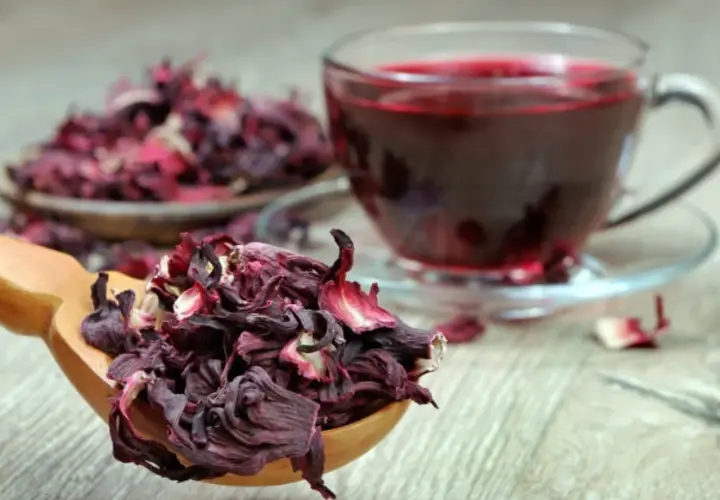 Cucharada de flor de jamaica seca junto a una taza de té rojo vibrante.