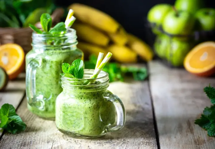 Batidos verdes refrescantes con espirulina, que es un superalimento, adornados con menta. Plátanos, naranjas y manzanas verdes en el fondo.