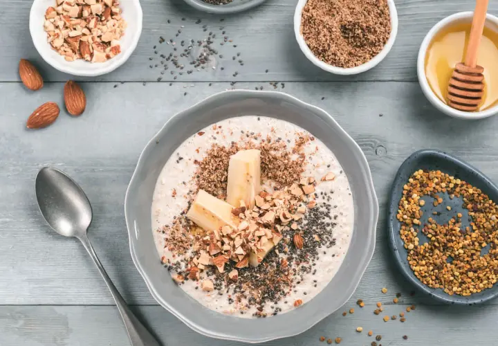 Un tazón de avena con plátano, almendras picadas, semillas de chía y miel. Aprende como tomar avena para un desayuno nutritivo.