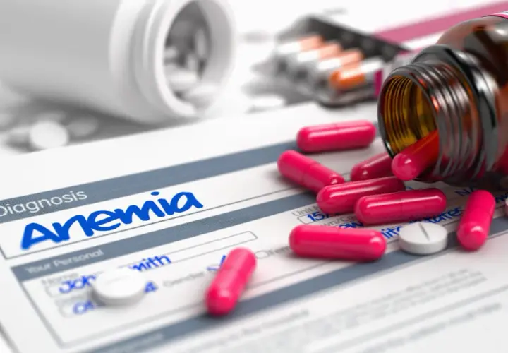 Pastillas rosas y blancas sobre un formulario de diagnóstico de anemia. Un frasco de suplemento de hierro derramado.