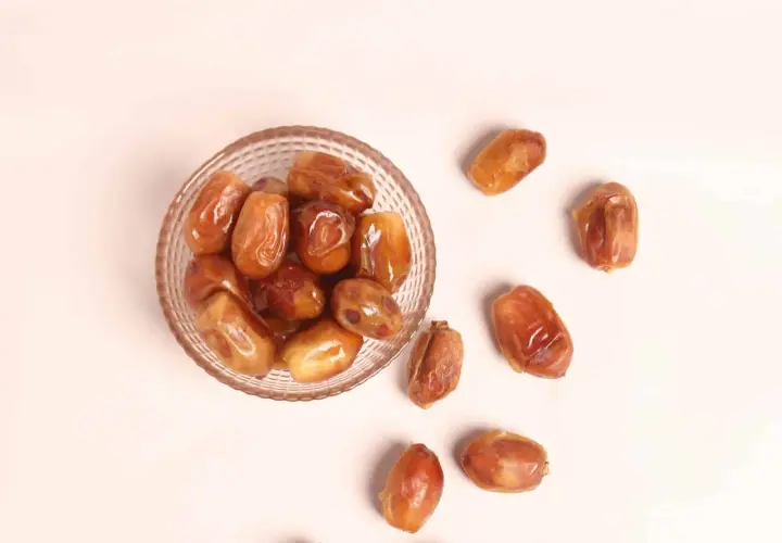 Un cuenco de cristal lleno de dátiles jugosos y otros esparcidos alrededor, destacando sus nutritivas propiedades.