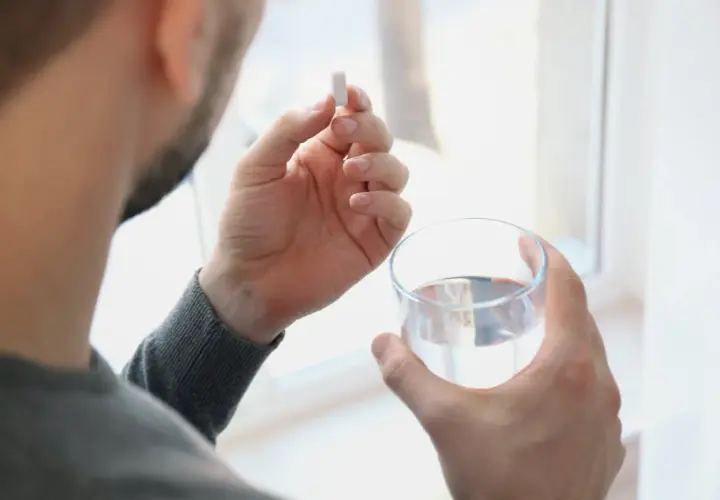 Hombre toma un comprimido de ácido fólico con un vaso de agua.