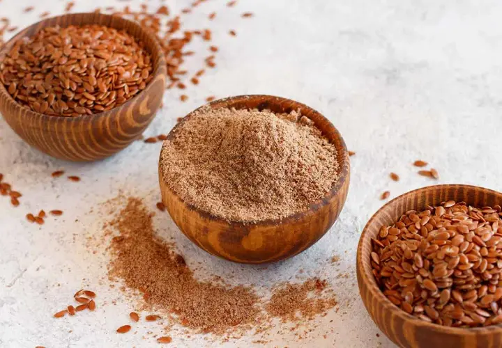 Tres cuencos de madera con semillas de lino enteras y molidas. Las semillas de lino son un superalimento versátil.