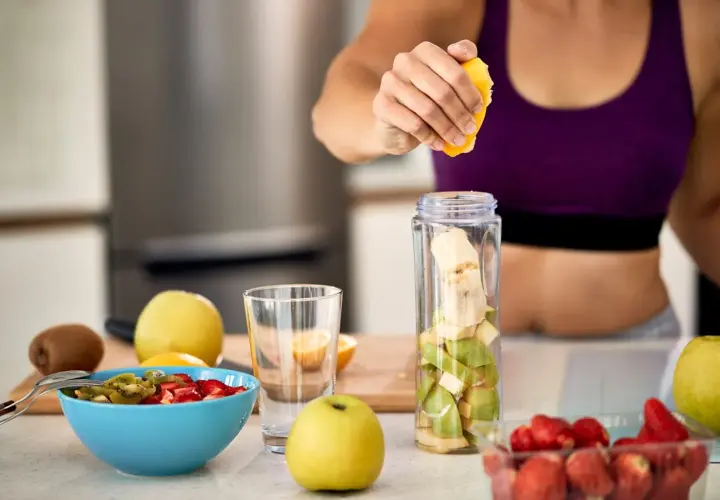 Mujer prepara batido de frutas. Ideal para saber **que tomar para las agujetas** y recuperarse tras el ejercicio.