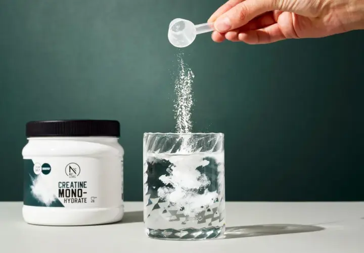 Un tarro de creatina monohidratada junto a un vaso donde se disuelve el polvo. Ideal para quienes buscan mejorar su rendimiento y apoyar la creatina para adelgazar.