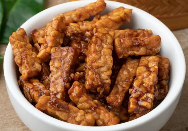 Trozos de tempeh que es, glaseados y dorados, servidos en un cuenco blanco.