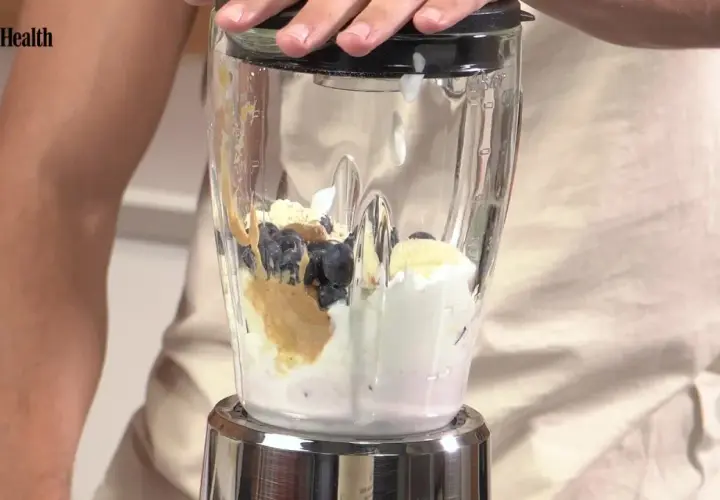 Ingredientes para batidos de proteínas: arándanos, plátano, crema y mantequilla de cacahuete en una licuadora.