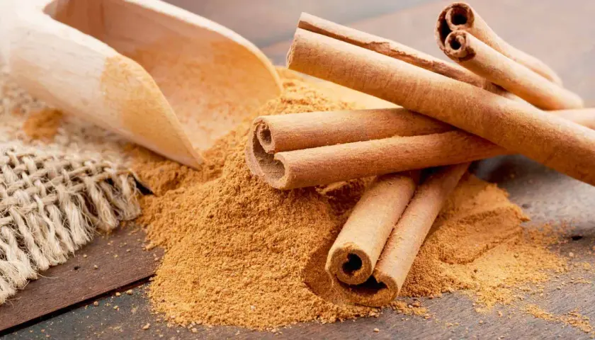 Palitos de canela y canela molida en una cuchara de madera. Descubre los 7 beneficios de la canela molida.