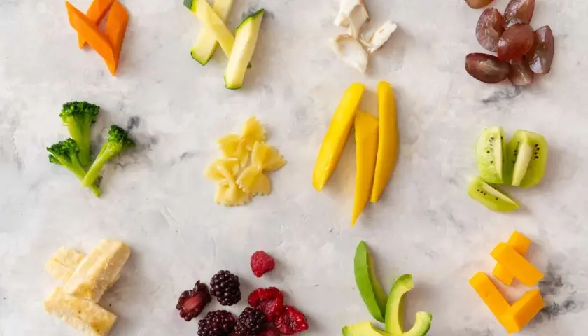 Variedad de alimentos cortados para blw bebe: zanahoria, calabacín, brócoli, pasta, mango, aguacate, plátano, bayas, kiwi y queso.