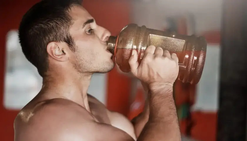 Hombre bebiendo de una gran botella, preparándose para un pre entreno fuerte.