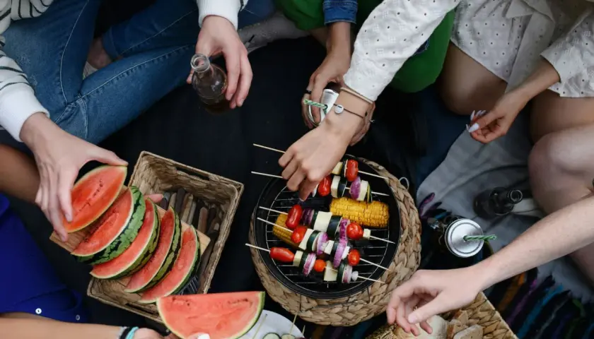 Disfrutando de una barbacoa vegetariana al aire libre con amigos, con brochetas de verduras a la parrilla, sandía y pan.