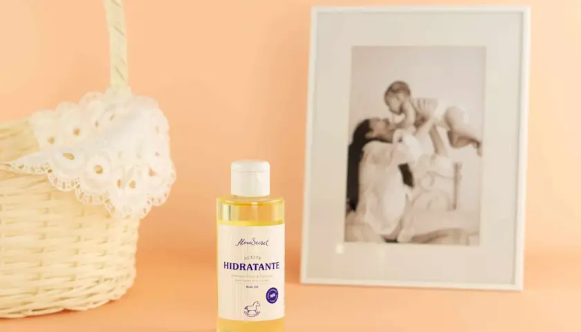 Aceite hidratante de almendras, ideal para el cuidado de la piel durante el embarazo. Cesta de mimbre y foto familiar al fondo.