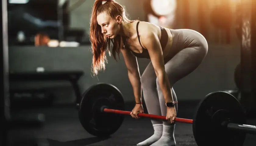 Mujer concentrada levanta una barra pesada, demostrando fuerza y dedicación en su entrenamiento para ganar masa muscular.