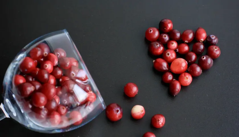 Arándanos rojos en forma de corazón y en una copa, ideales para infusiones y para saber para qué sirve la gayuba.