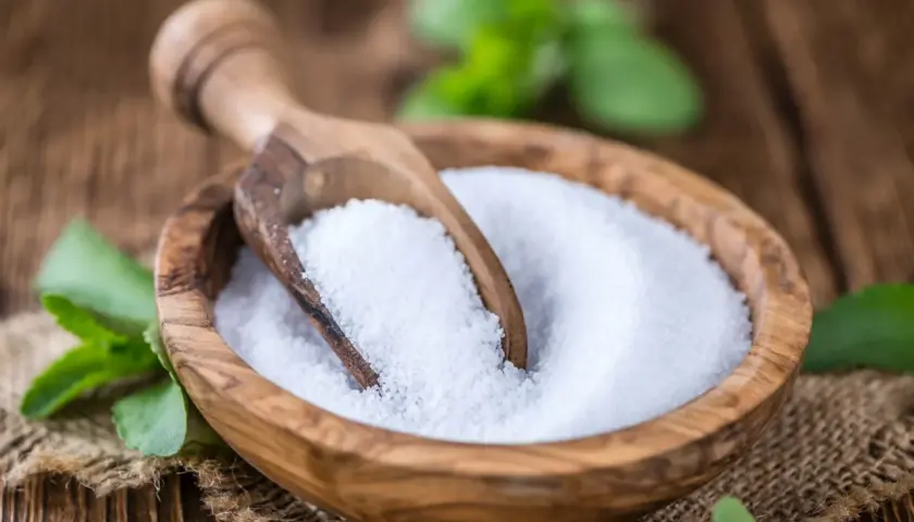 Tazón de madera con azúcar de stevia y cuchara. Las hojas verdes de stevia alrededor nos recuerdan que es la stevia, un edulcorante natural.
