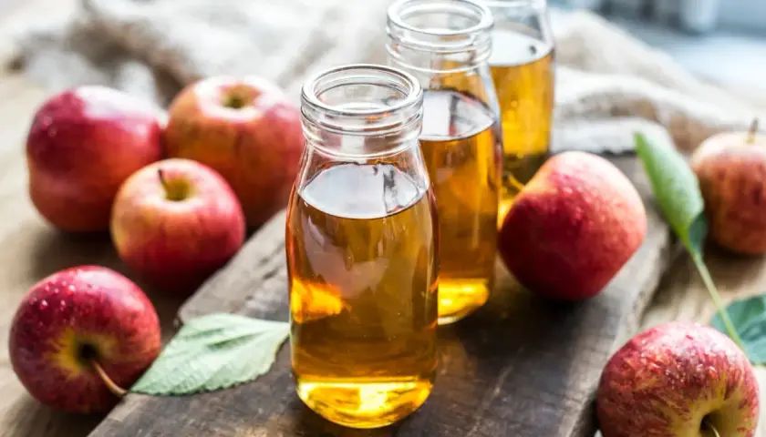 Botellas de vinagre de manzana, destacando sus propiedades naturales. Manzanas rojas frescas rodean el líquido dorado.