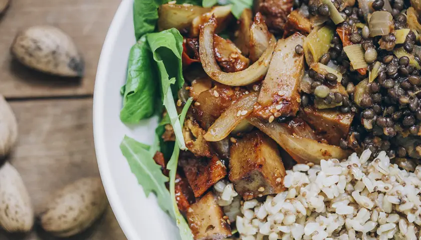 Un plato con seitan que es una proteína vegetal deliciosa, lentejas, arroz integral y hojas verdes.
