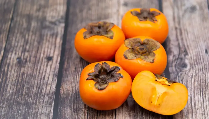 Caquis sobre una mesa de madera. Estos son algunos alimentos que estriñen, ¡pero deliciosos!