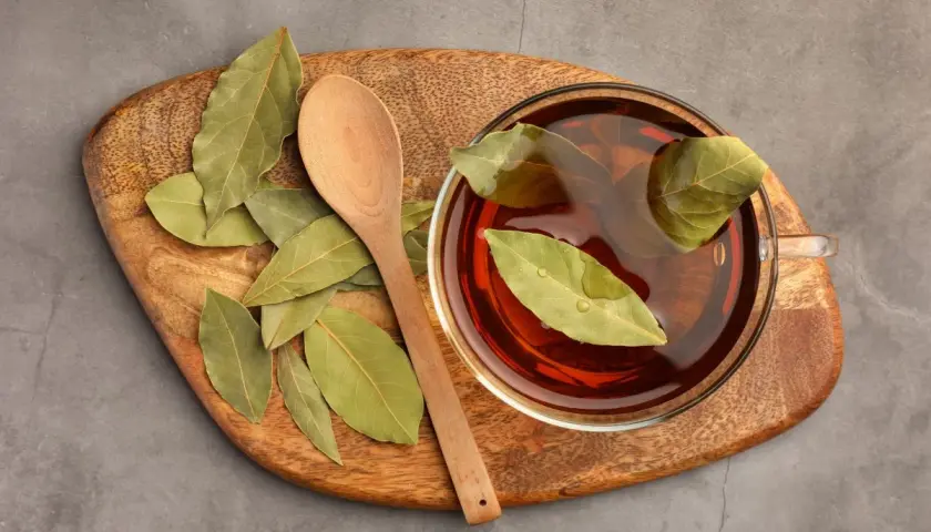 Taza de infusión de laurel con hojas flotando, junto a una cuchara de madera sobre una tabla rústica.