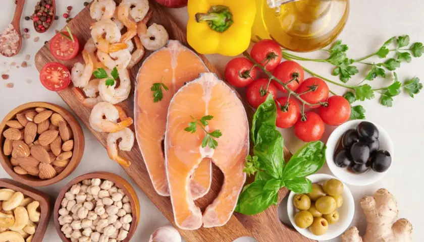 Salmón, camarones, almendras, garbanzos y aceitunas son algunos de los alimentos con yodo que se ven en la imagen, junto a tomates, pimientos y hierbas.