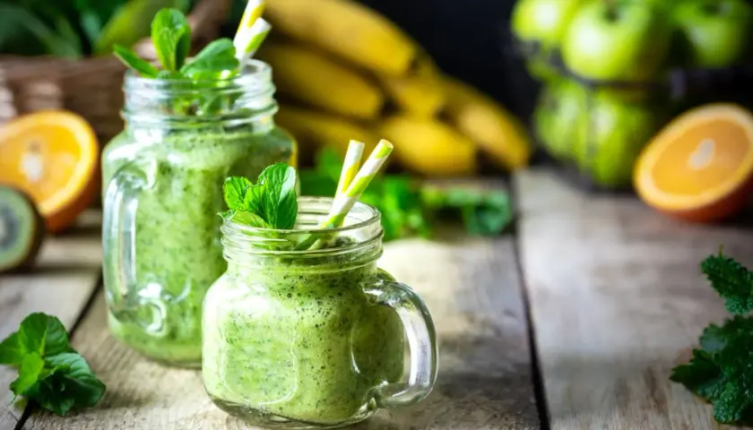Batidos verdes refrescantes con espirulina, que es un superalimento, adornados con menta. Plátanos, naranjas y manzanas verdes en el fondo.
