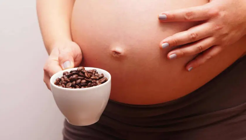 Una mujer embarazada sostiene una taza de granos de café. El café y el embarazo son un tema delicado.