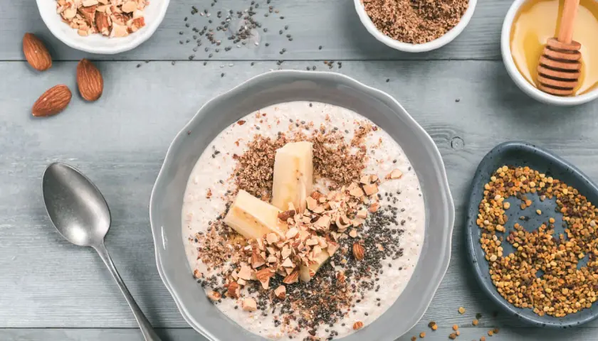 Un tazón de avena con plátano, almendras picadas, semillas de chía y miel. Aprende como tomar avena para un desayuno nutritivo.