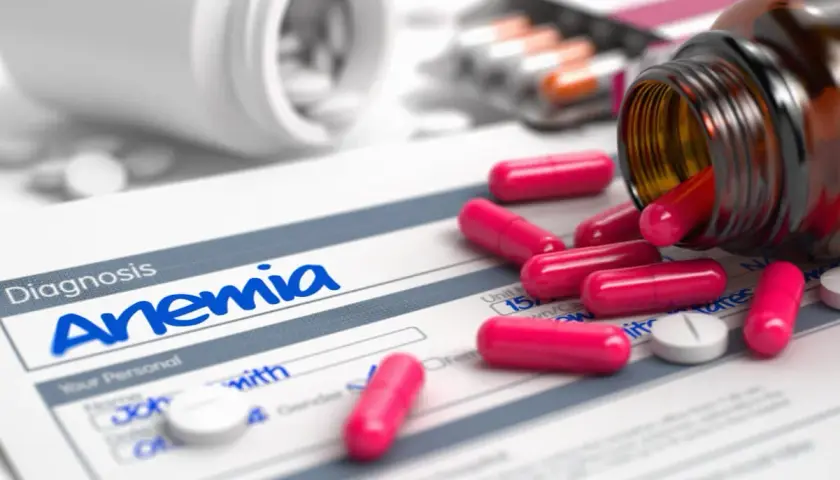 Pastillas rosas y blancas sobre un formulario de diagnóstico de anemia. Un frasco de suplemento de hierro derramado.