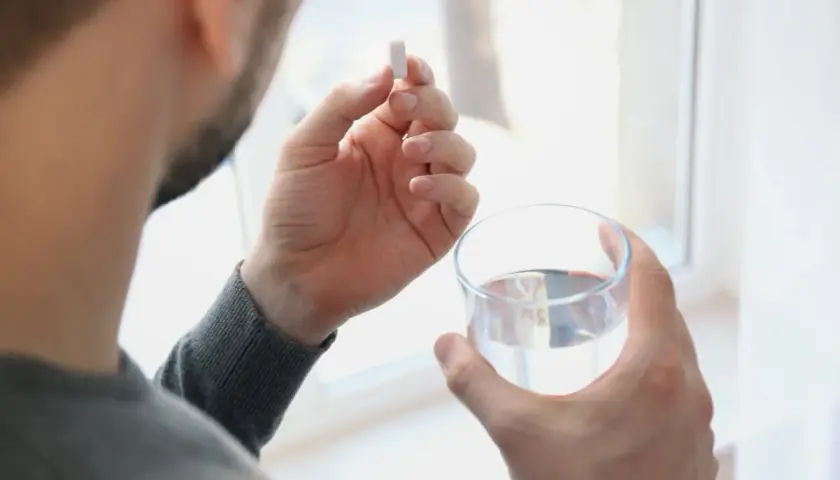 Hombre toma un comprimido de ácido fólico con un vaso de agua.