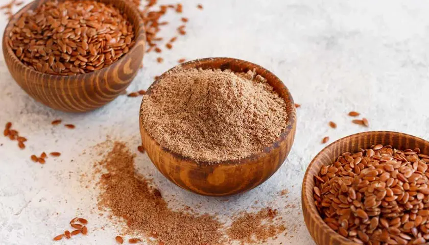 Tres cuencos de madera con semillas de lino enteras y molidas. Las semillas de lino son un superalimento versátil.