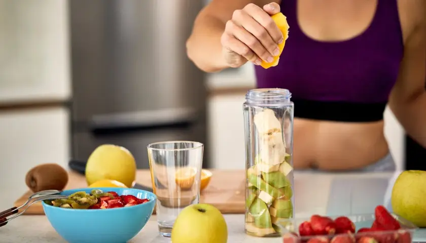 Mujer prepara batido de frutas. Ideal para saber **que tomar para las agujetas** y recuperarse tras el ejercicio.