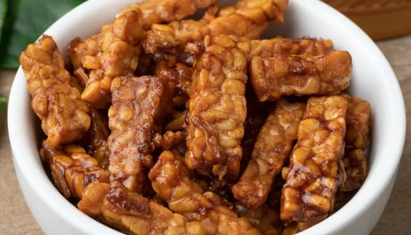 Trozos de tempeh que es, glaseados y dorados, servidos en un cuenco blanco.