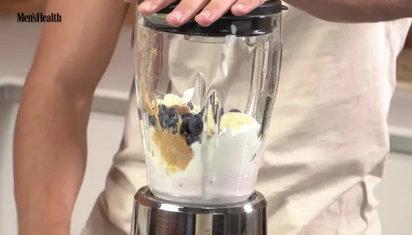 Ingredientes para batidos de proteínas: arándanos, plátano, crema y mantequilla de cacahuete en una licuadora.