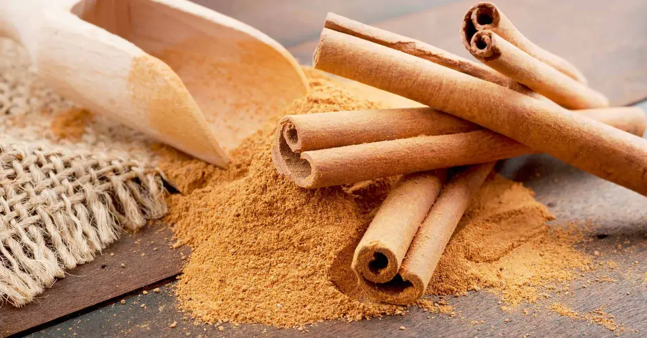 Palitos de canela y canela molida en una cuchara de madera. Descubre los 7 beneficios de la canela molida.