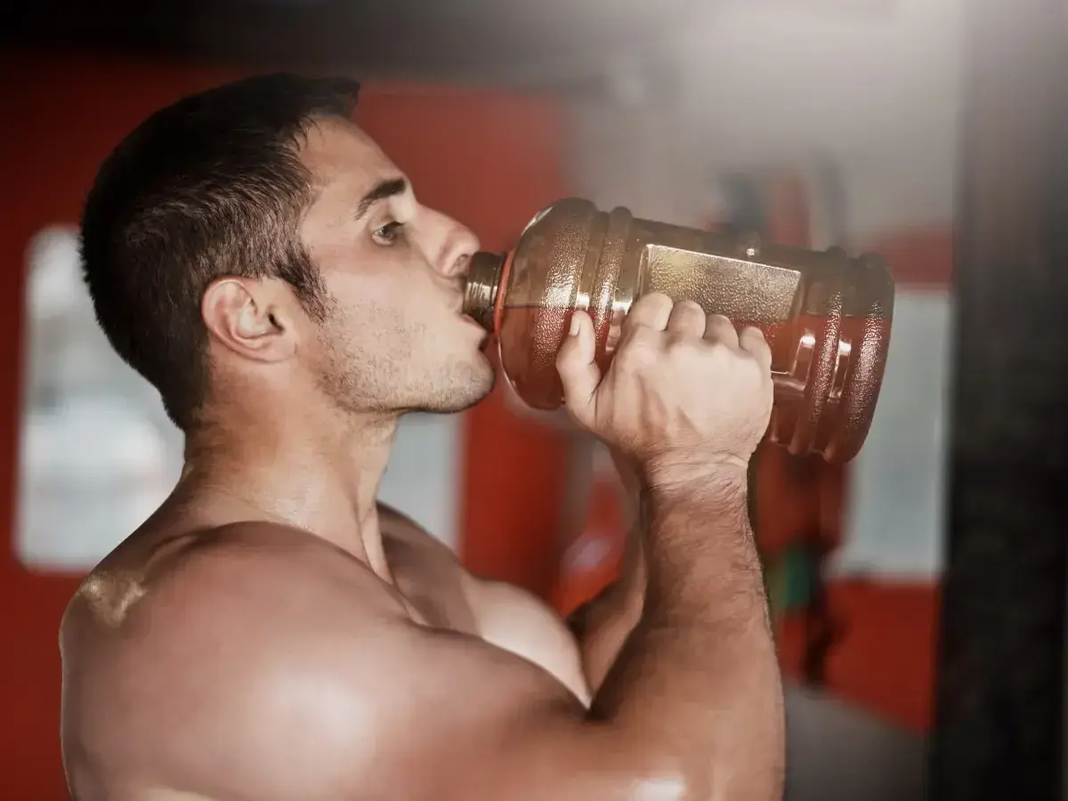 Hombre bebiendo de una gran botella, preparándose para un pre entreno fuerte.