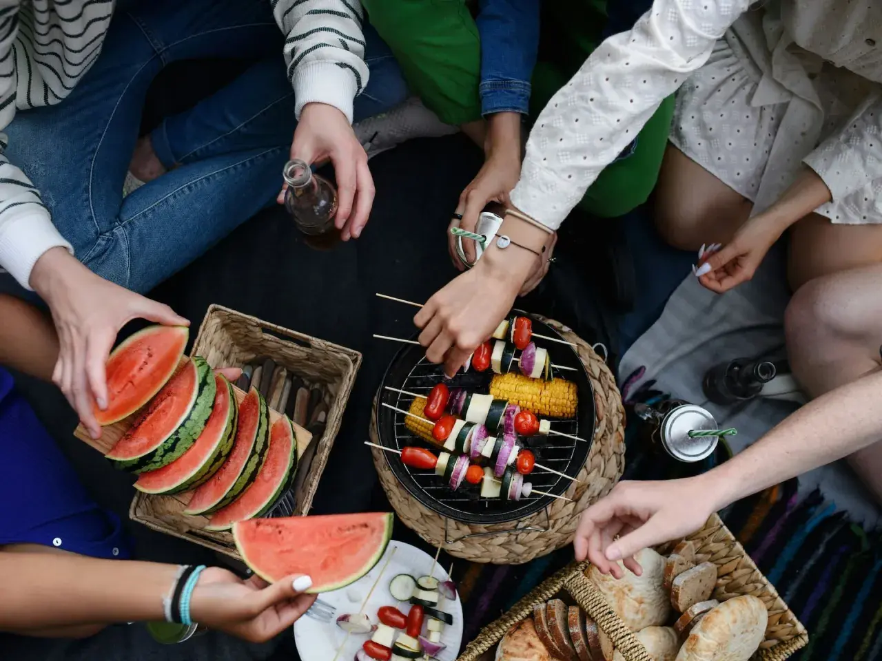 Disfrutando de una barbacoa vegetariana al aire libre con amigos, con brochetas de verduras a la parrilla, sandía y pan.