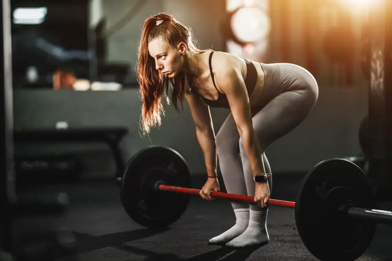 Mujer concentrada levanta una barra pesada, demostrando fuerza y dedicación en su entrenamiento para ganar masa muscular.