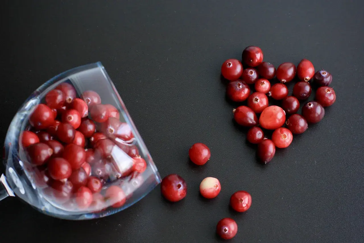 Arándanos rojos en forma de corazón y en una copa, ideales para infusiones y para saber para qué sirve la gayuba.