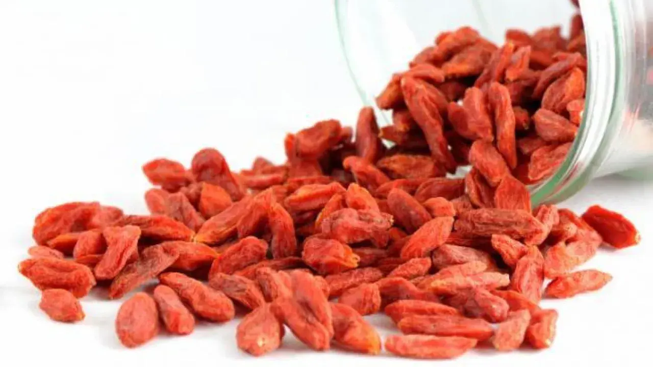 Un frasco de vidrio derrama bayas de goji, destacando sus vibrantes bayas rojas y sus innumerables propiedades beneficiosas.