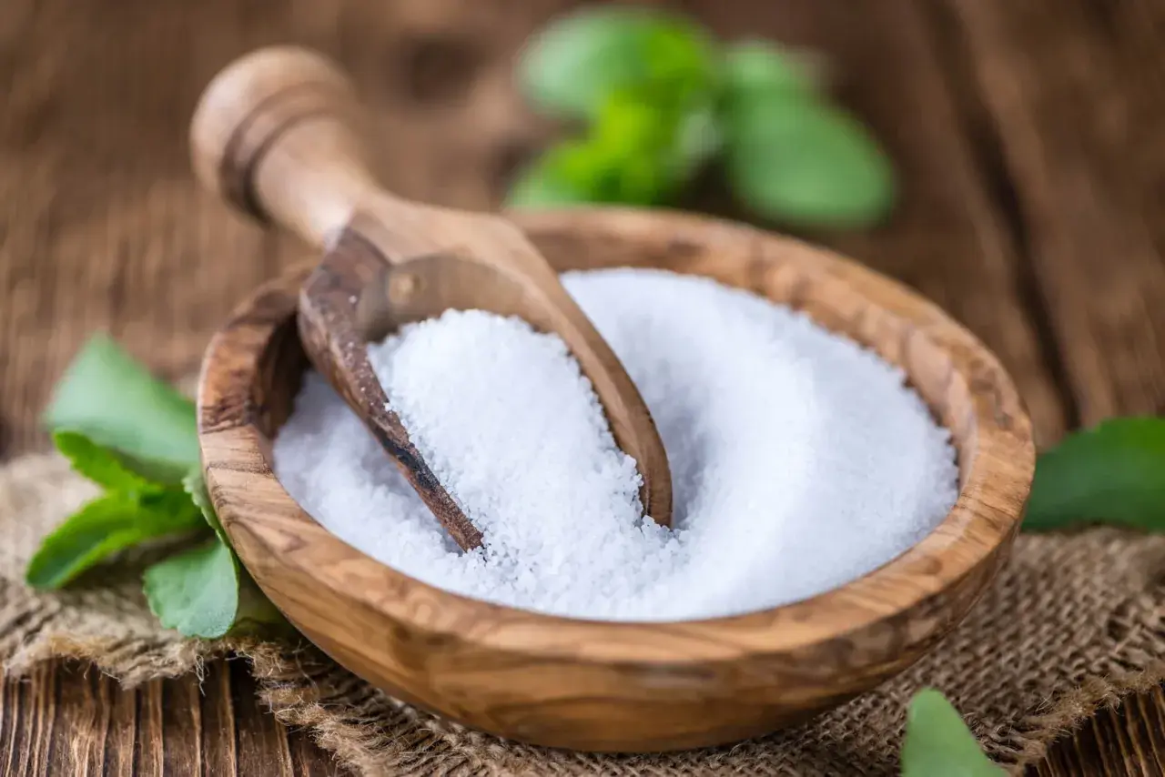 Tazón de madera con azúcar de stevia y cuchara. Las hojas verdes de stevia alrededor nos recuerdan que es la stevia, un edulcorante natural.