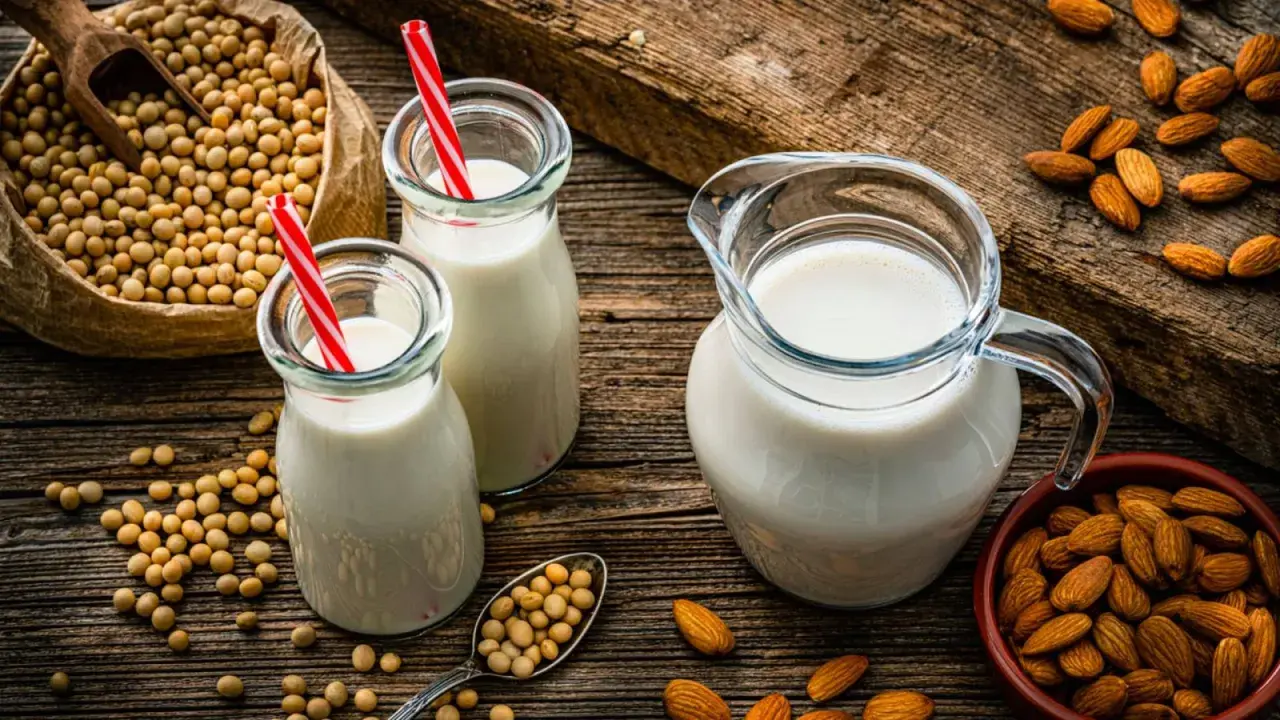 Botellas y jarra con bebida vegetal, junto a un saco de soja y almendras.