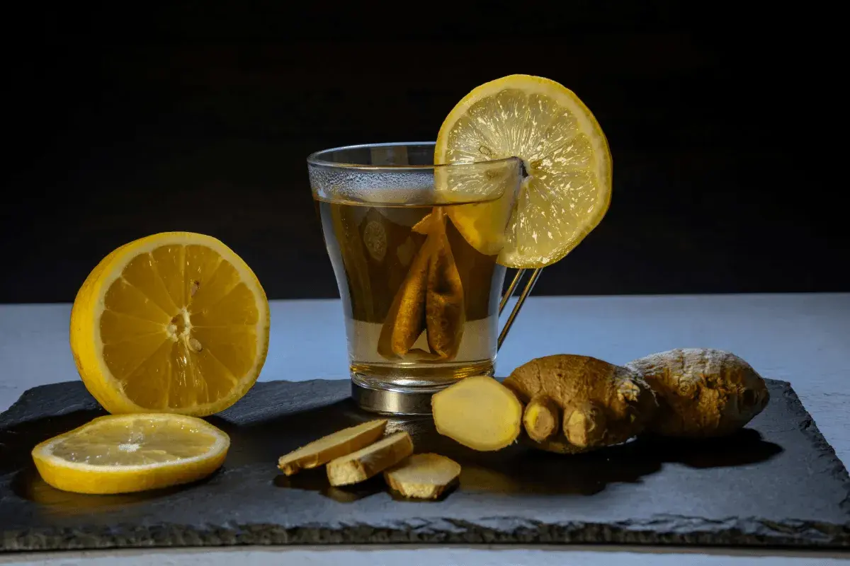 Un vaso de té con limón y jengibre, acompañado de rodajas de limón y trozos de jengibre fresco. Un shot de jengibre para revitalizar.