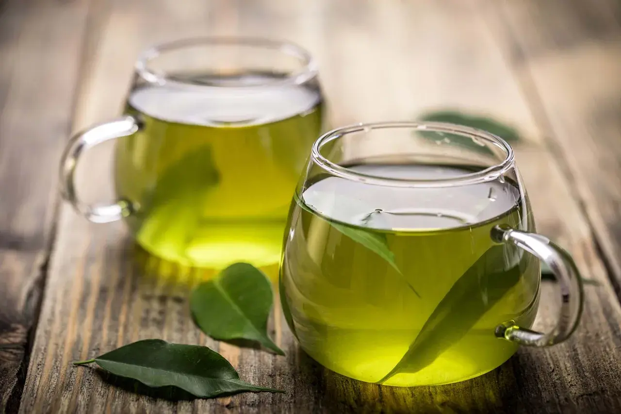 Dos tazas de té verde en vasos de cristal, con hojas flotando. Descubre para qué sirve el té verde y sus beneficios.