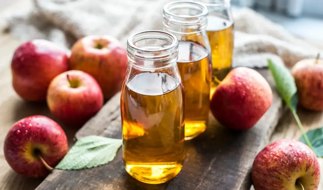 Botellas de vinagre de manzana, destacando sus propiedades naturales. Manzanas rojas frescas rodean el líquido dorado.