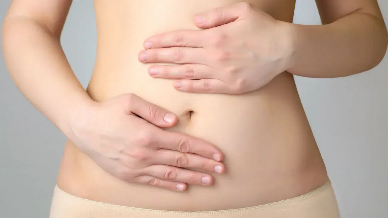 Manos sobre el abdomen, sugiriendo dolor o malestar, y la necesidad de evitar alimentos prohibidos para el estómago inflamado.
