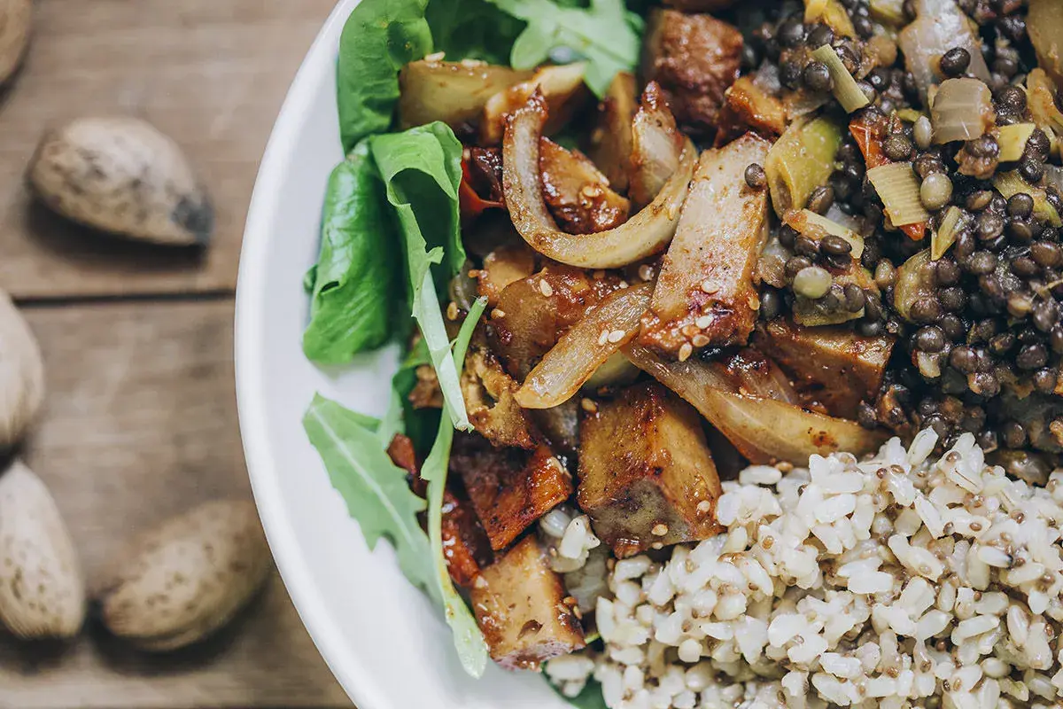 Un plato con seitan que es una proteína vegetal deliciosa, lentejas, arroz integral y hojas verdes.