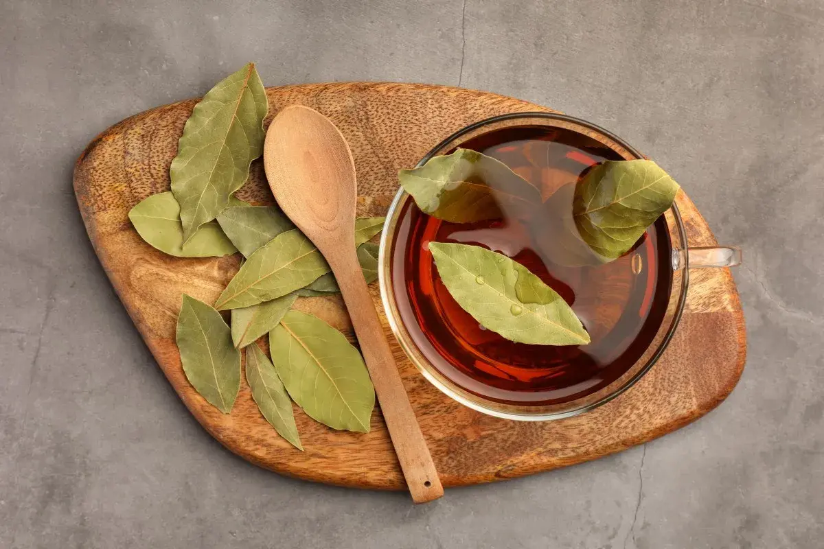 Taza de infusión de laurel con hojas flotando, junto a una cuchara de madera sobre una tabla rústica.