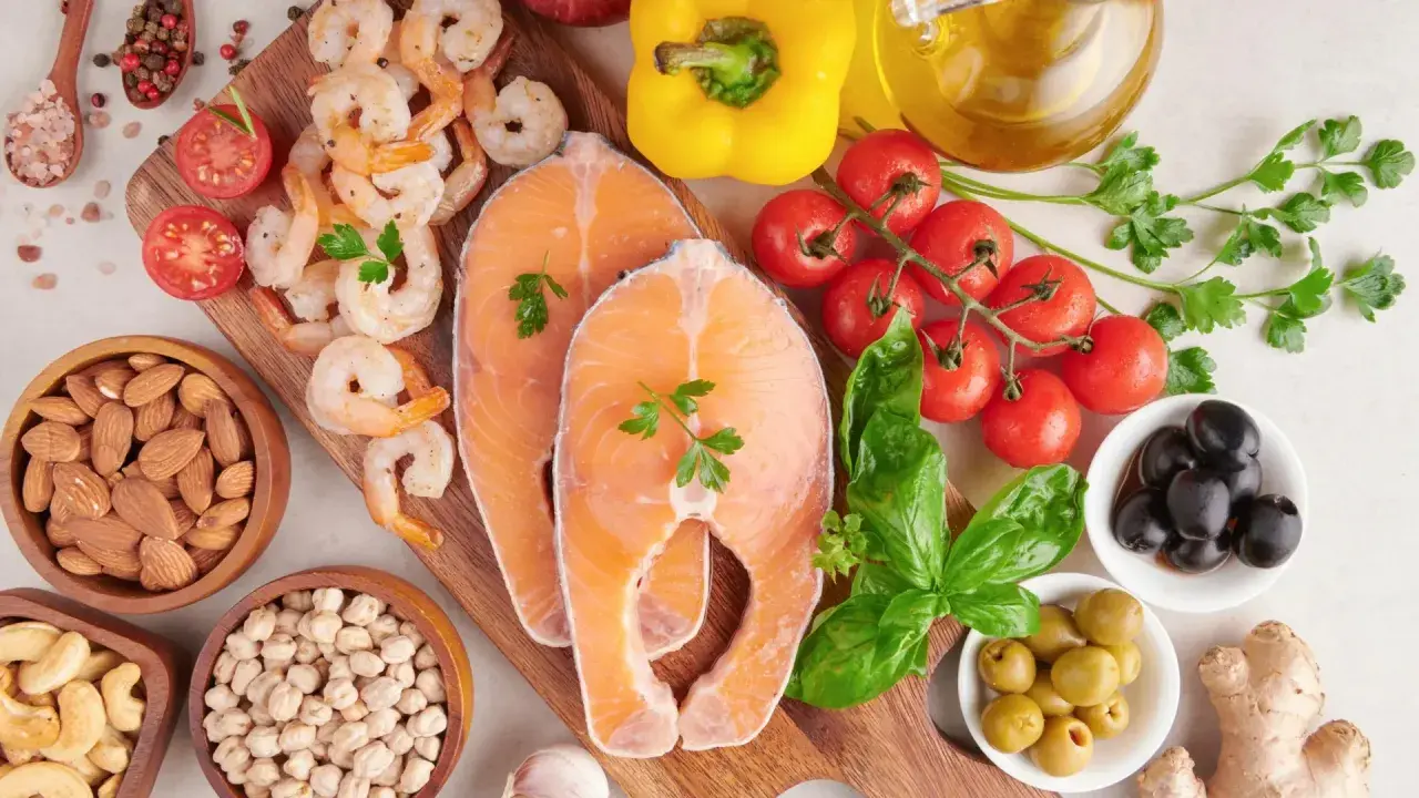 Salmón, camarones, almendras, garbanzos y aceitunas son algunos de los alimentos con yodo que se ven en la imagen, junto a tomates, pimientos y hierbas.