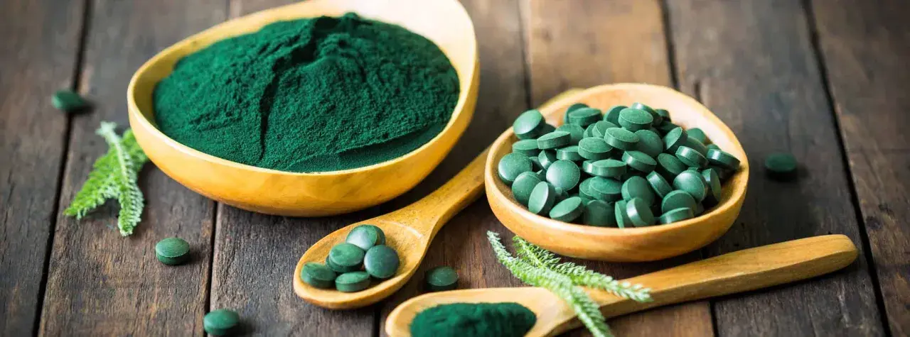 Polvo y pastillas verdes vibrantes, que muestran qué es la chlorella, en cuencos de madera y cucharas sobre una superficie rústica.